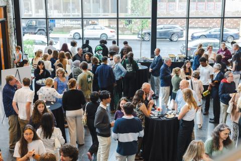 Students, faculty, and family gather in a lobby around tables.